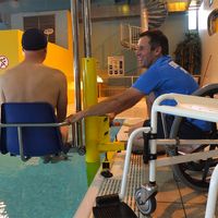 Chaise ascenseur de mise à l'eau avec éducateur sportif aidant à la mise à l'eau